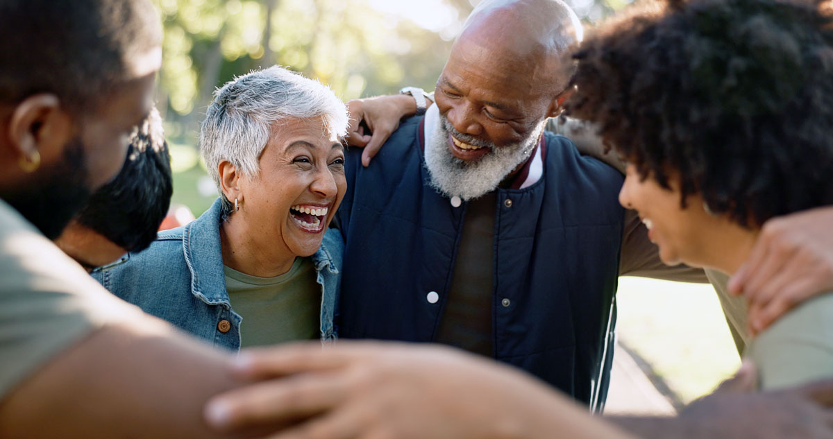 A multigenerational group of community members laughing and embracing one another outdoors