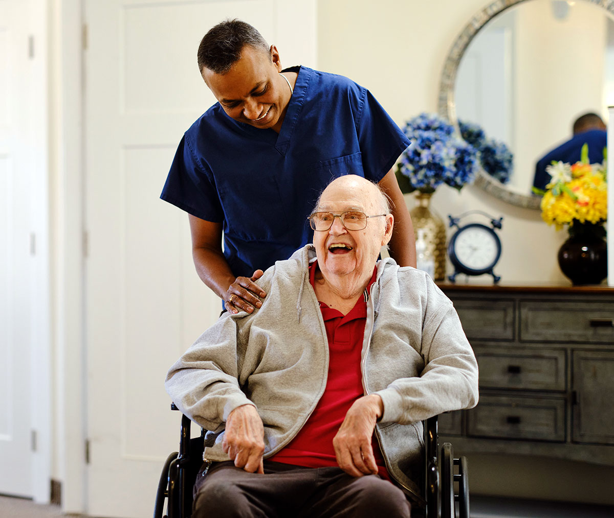 A care aide in navy scrubs sharing a joyful moment with an elderly client in a wheelchair at home