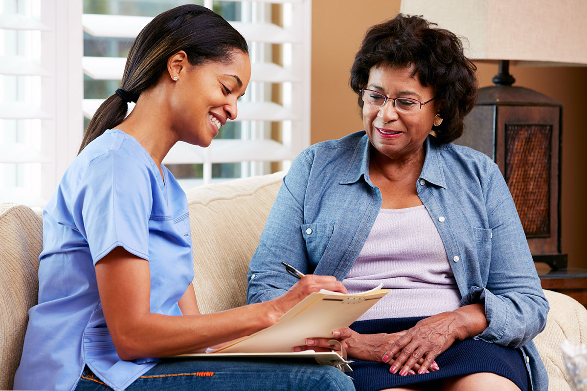 A care provider reviewing a care plan with an older woman at home, seated together on a couch