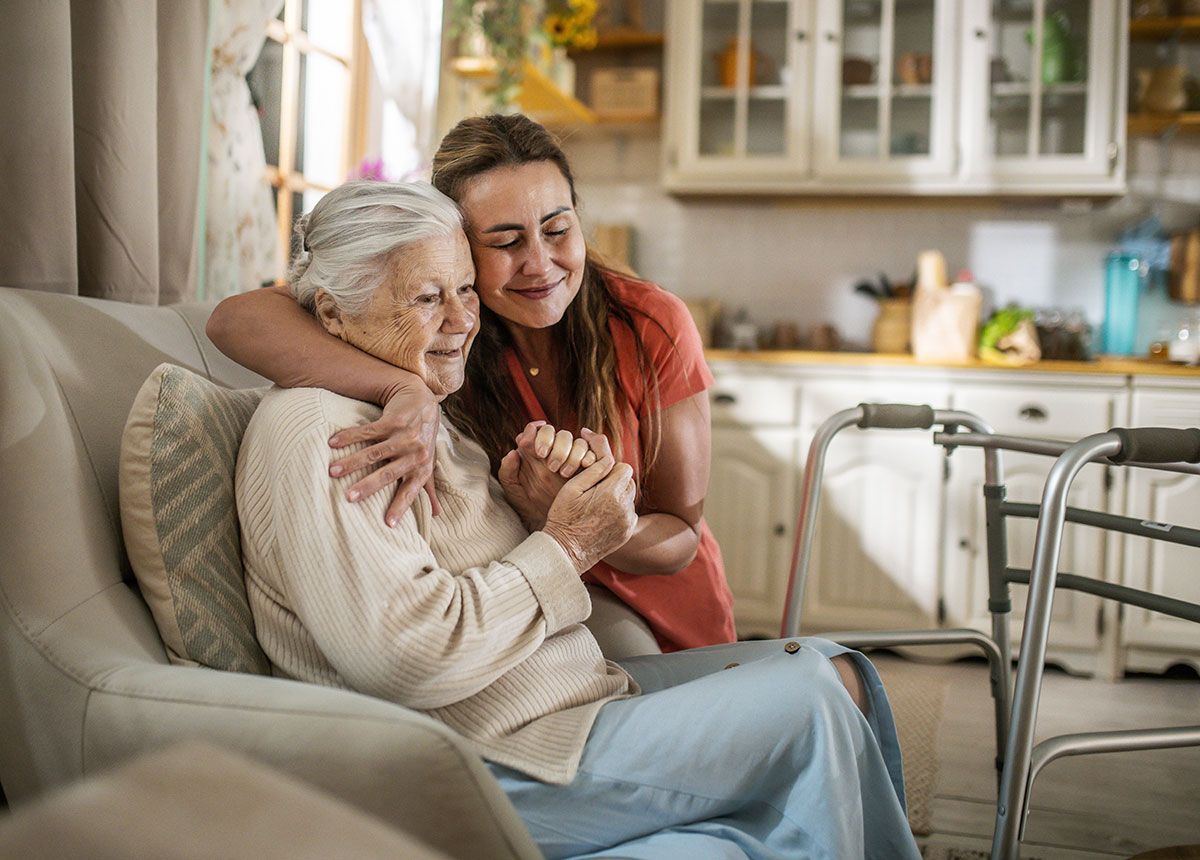 A daughter embracing her elderly mother at home, holding her hands